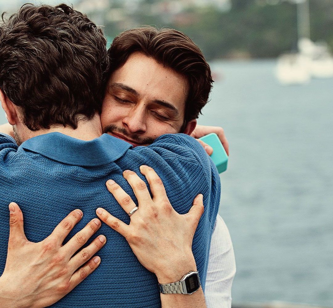 Two men share an embrace on a harbor waterfront